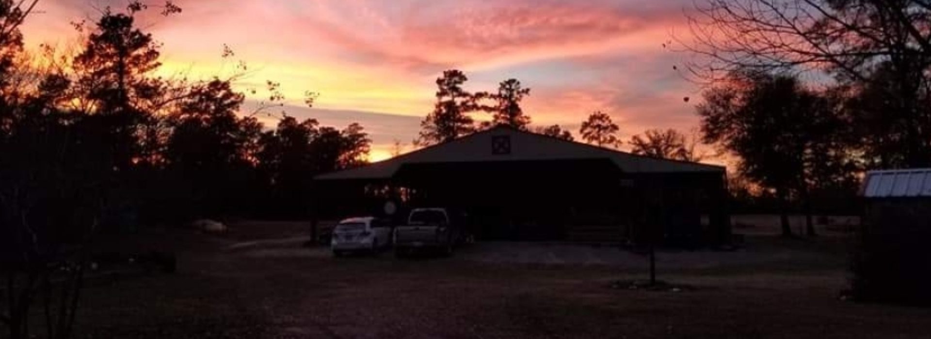 A sunset over a building with two cars parked in front of it.