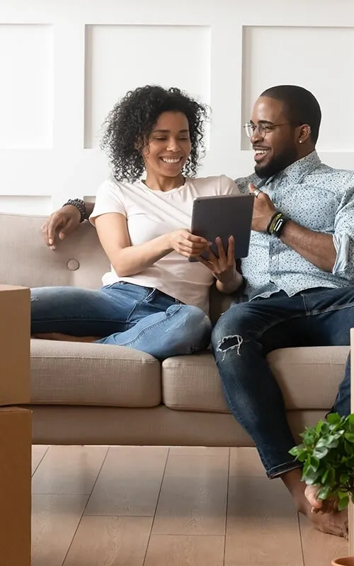 A man and woman sitting on the couch looking at an ipad.