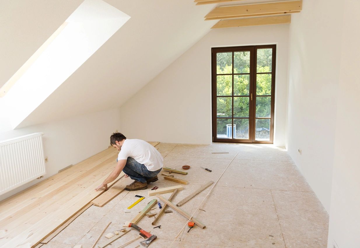 A man laying down wood in an unfinished room.